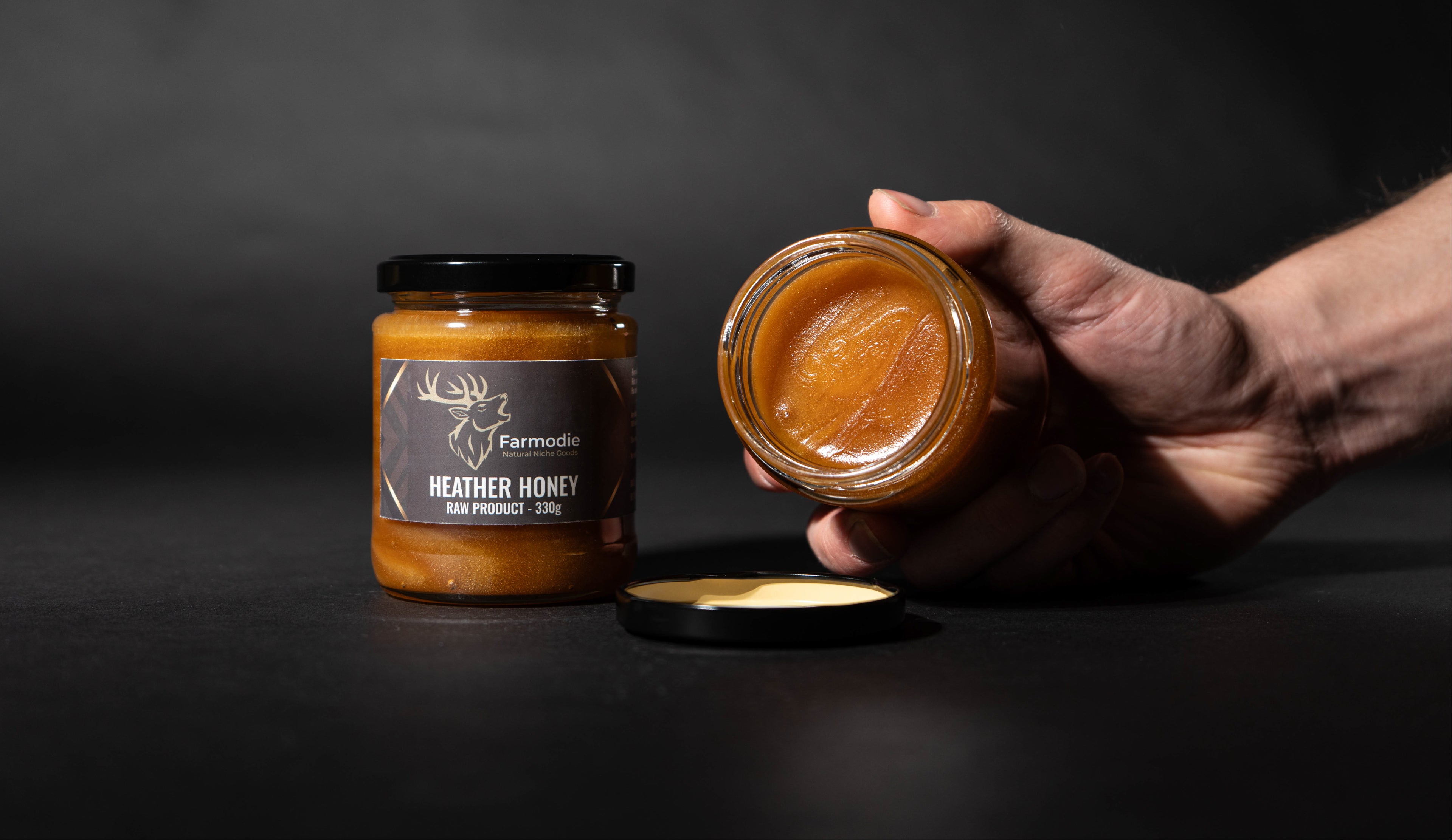 Hand holding a jar of Heather Honey with another jar on a dark background